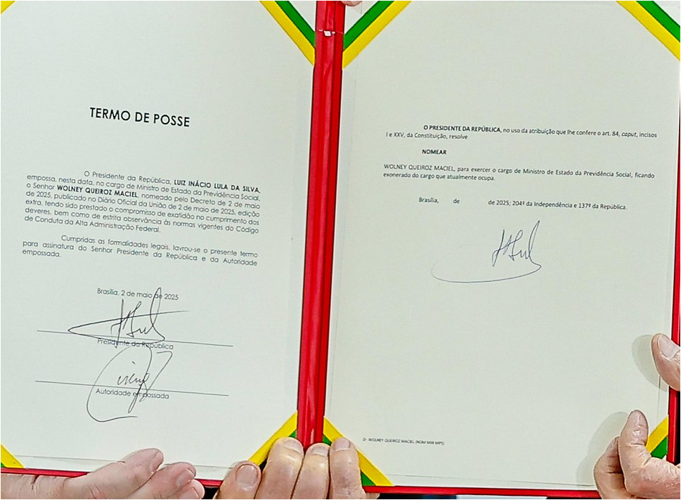 Documento oficial de posse assinado, com moldura vermelha e bordas decoradas com faixas verdes e amarelas. O texto, intitulado “Termo de Posse”, nomeia Wolney Queiroz Maciel como Ministro de Estado da Previdência Social, assinado pelo presidente Luiz Inácio Lula da Silva.